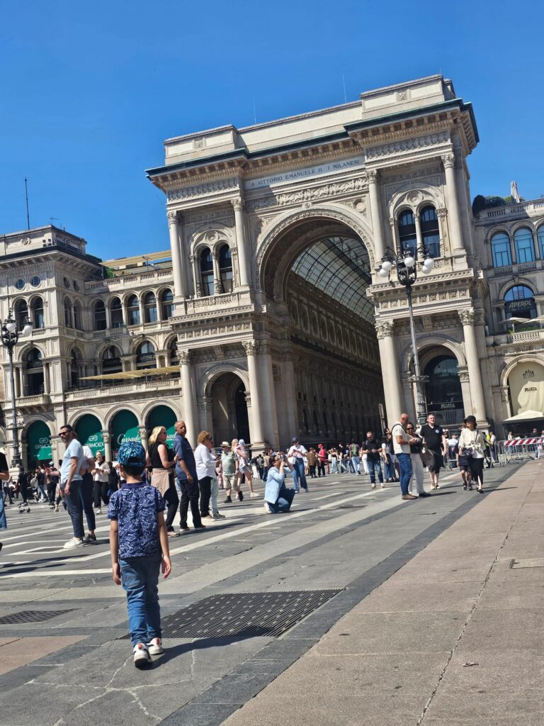 Entrance of the Galleria Vittorio Emanuele II in Milan with crowds walking across Piazza del Duomo