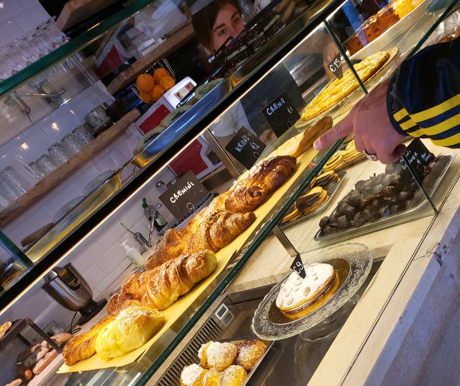 Pastry case in Italian bakery with croissants and desserts.