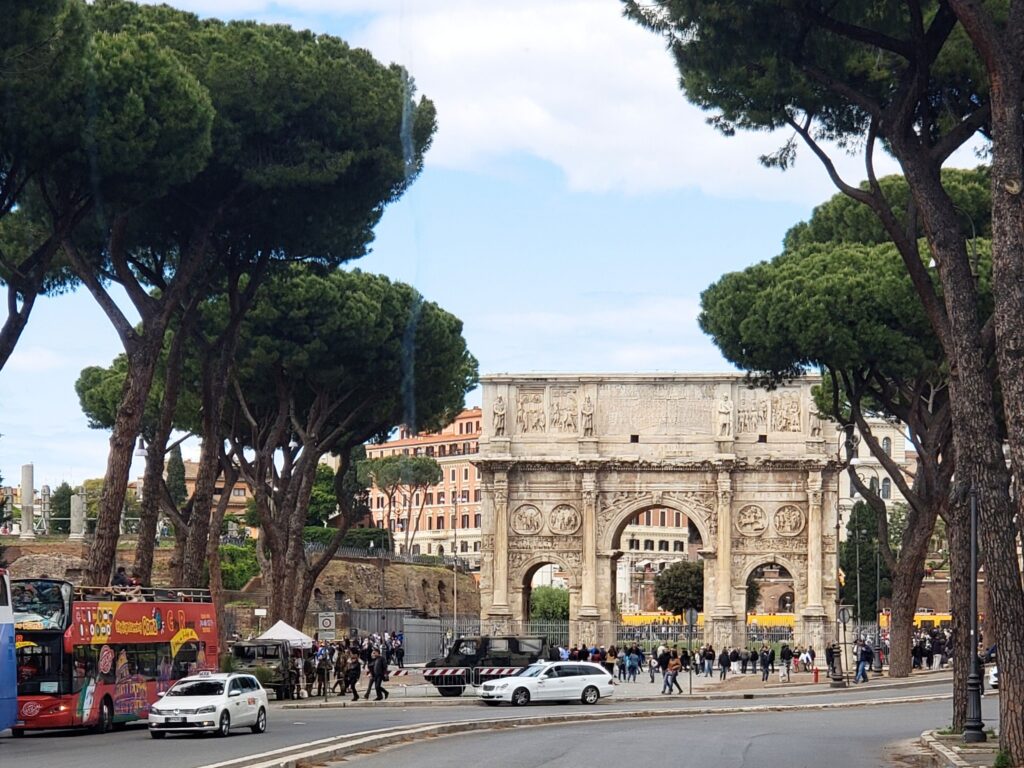 The ancient Arch of Constantine framed by Roman pine trees with the Colosseum in the background.