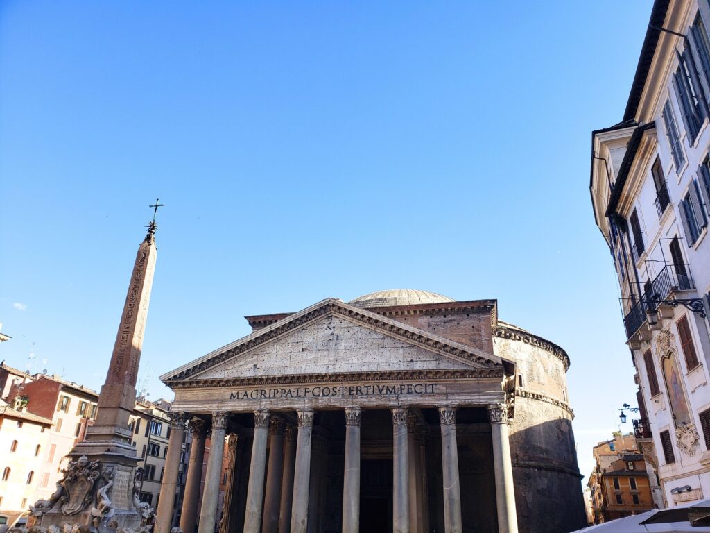 Exterior view of the Pantheon in Rome with its massive granite columns and the obelisk in the foreground.