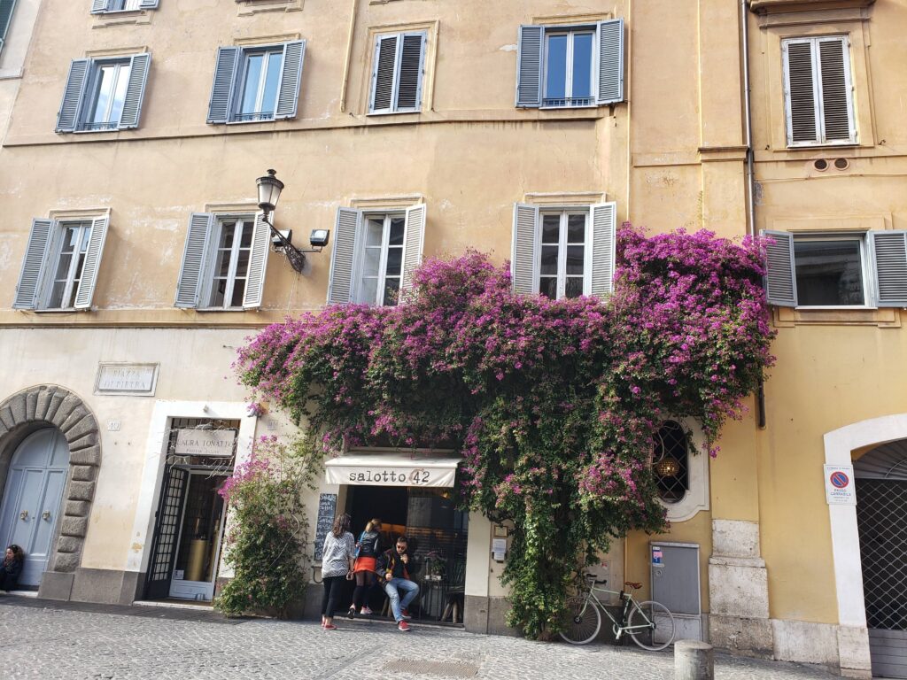 A beautiful ochre building in Rome covered in vibrant purple bougainvillea flowers.