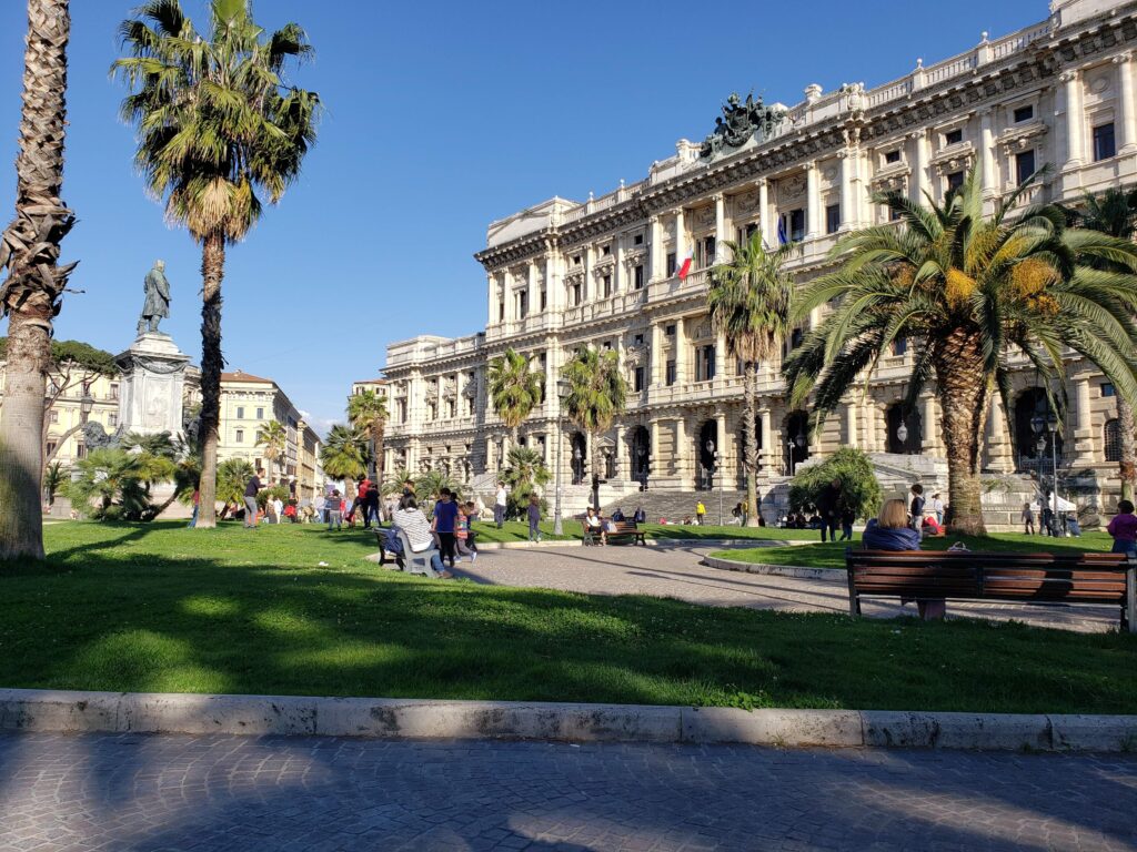 The Palace of Justice in Rome featuring bronze statues and palm trees in the foreground.