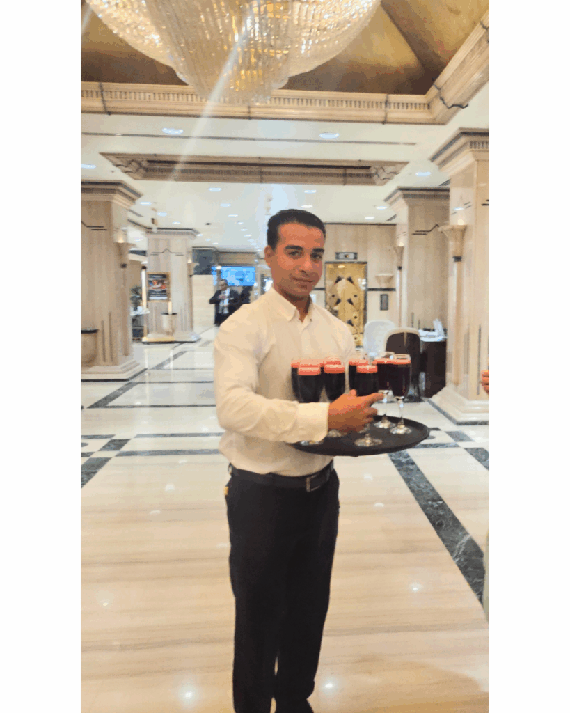 A hotel server presenting a tray of bright red hibiscus tea glasses in a marble lobby.