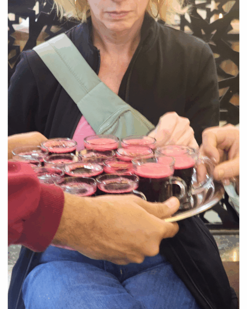Hands reaching for small glasses of Karkadeh on a silver tray during a welcome service.