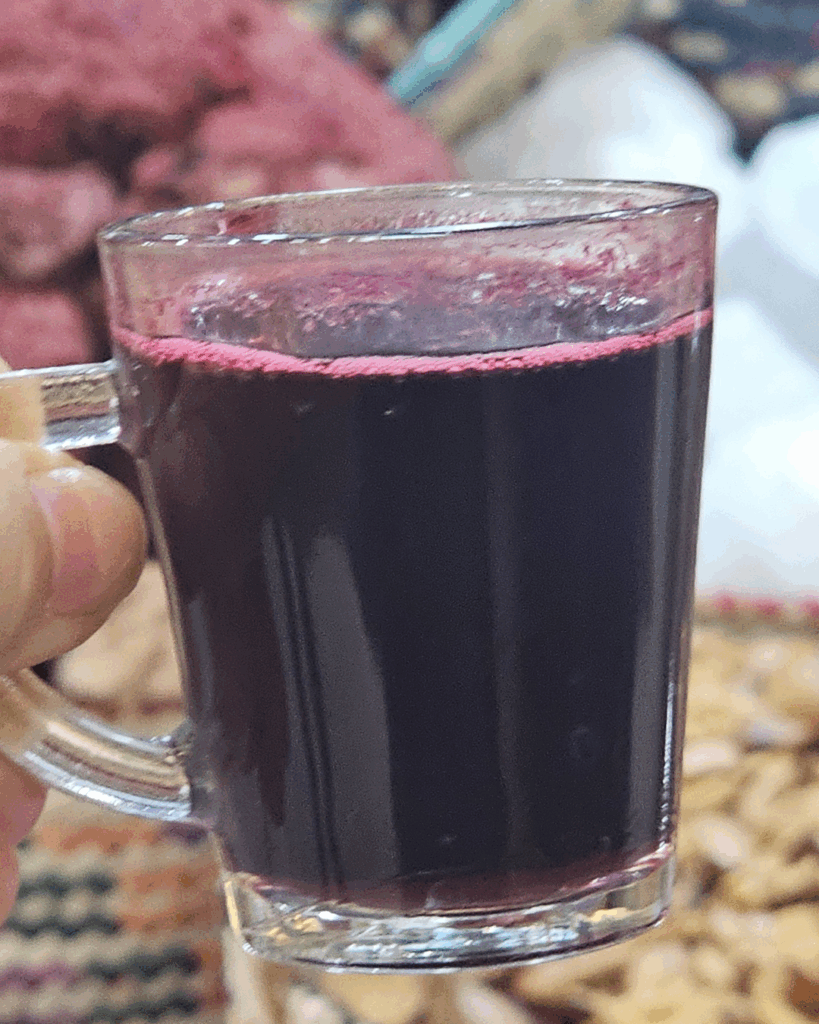 Close-up of a small glass of dark purple Karkadeh held inside an Egyptian spice market.