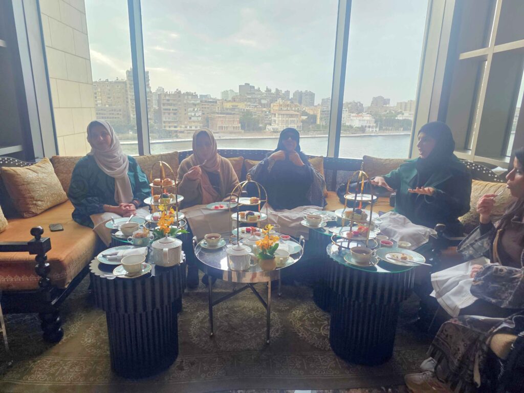 A group of Egyptian women enjoying afternoon tea with tiered trays and Nile River views behind them.