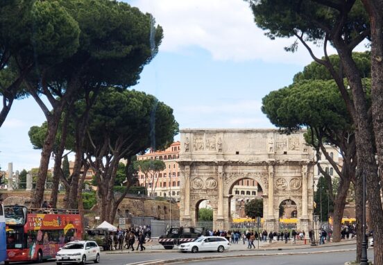 The ancient Arch of Constantine framed by Roman pine trees with the Colosseum in the background.