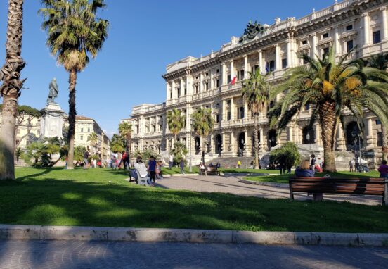 The Palace of Justice in Rome featuring bronze statues and palm trees in the foreground.