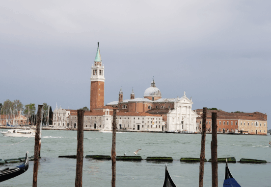 Horizontal "hero shot" of San Giorgio Maggiore from across the water, with the gondola prows in the foreground.