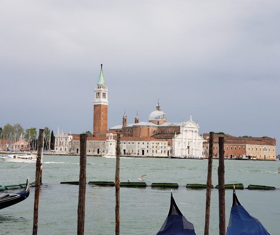 Horizontal "hero shot" of San Giorgio Maggiore from across the water, with the gondola prows in the foreground.