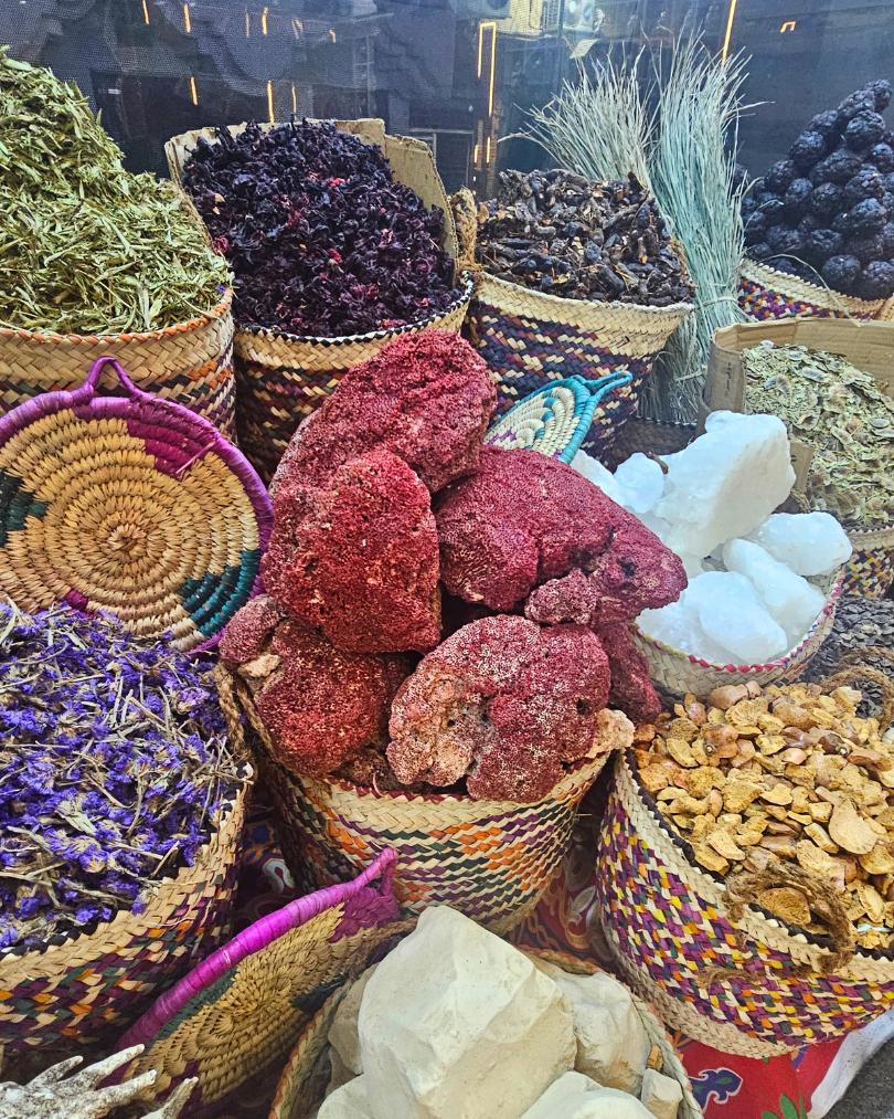 Colorful woven baskets filled with dried hibiscus petals, herbs, and spices in a traditional Egyptian market.